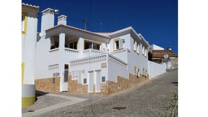 A white building with a stone base, a staircase, and a cobblestone street. - Casa Goncalito Ground floor (Bordeira)