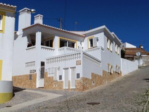 Un bâtiment blanc avec un socle en pierre, un escalier et une rue pavée.