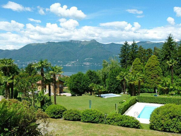A resort with a swimming pool, lush greenery, and a view of mountains and a lake.