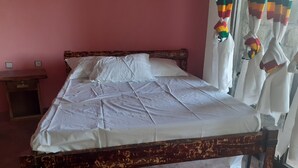 A bed with a white sheet, a wooden headboard, and a window with curtains. - Bethan Amba ecovillage (Lalibela)