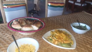 A table with a woven tablecloth, a basket of rolls, a bowl of fruit, and a bowl of food. - Bethan Amba ecovillage (Lalibela)