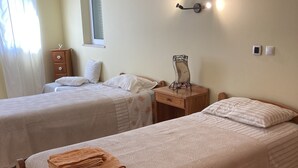 A room with two single beds, a wooden nightstand, a small cabinet, a red rug, and a wall-mounted light fixture. - Casa rustica, Apartment with balcony (Bordeira)