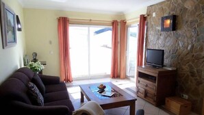A living room with a sofa, a coffee table, a TV on a wooden cabinet, and a stone wall. - Casa rustica, Apartment with balcony (Bordeira)