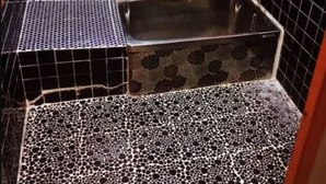 Un baño pequeño con piso de patrón blanco y negro, una bañera de metal y paredes cubiertas de azulejos negros.