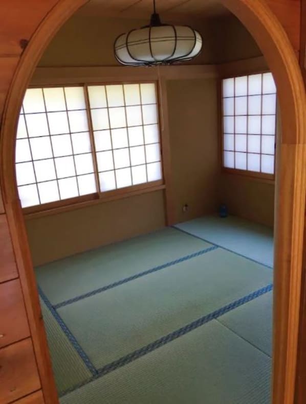 A traditional Japanese room with tatami flooring, shoji screens, and a hanging light fixture.