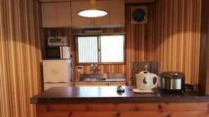 Una cocina compacta con paneles de madera, microondas, lavamanos y hervidor sobre la encimera.