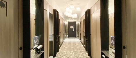 A hotel corridor with patterned flooring, mirrored doors, and a central chandelier.