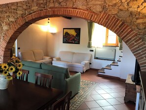 Una sala de estar con un arco de piedra, un sofá, una mesa de comedor con sillas y un cuadro en la pared.