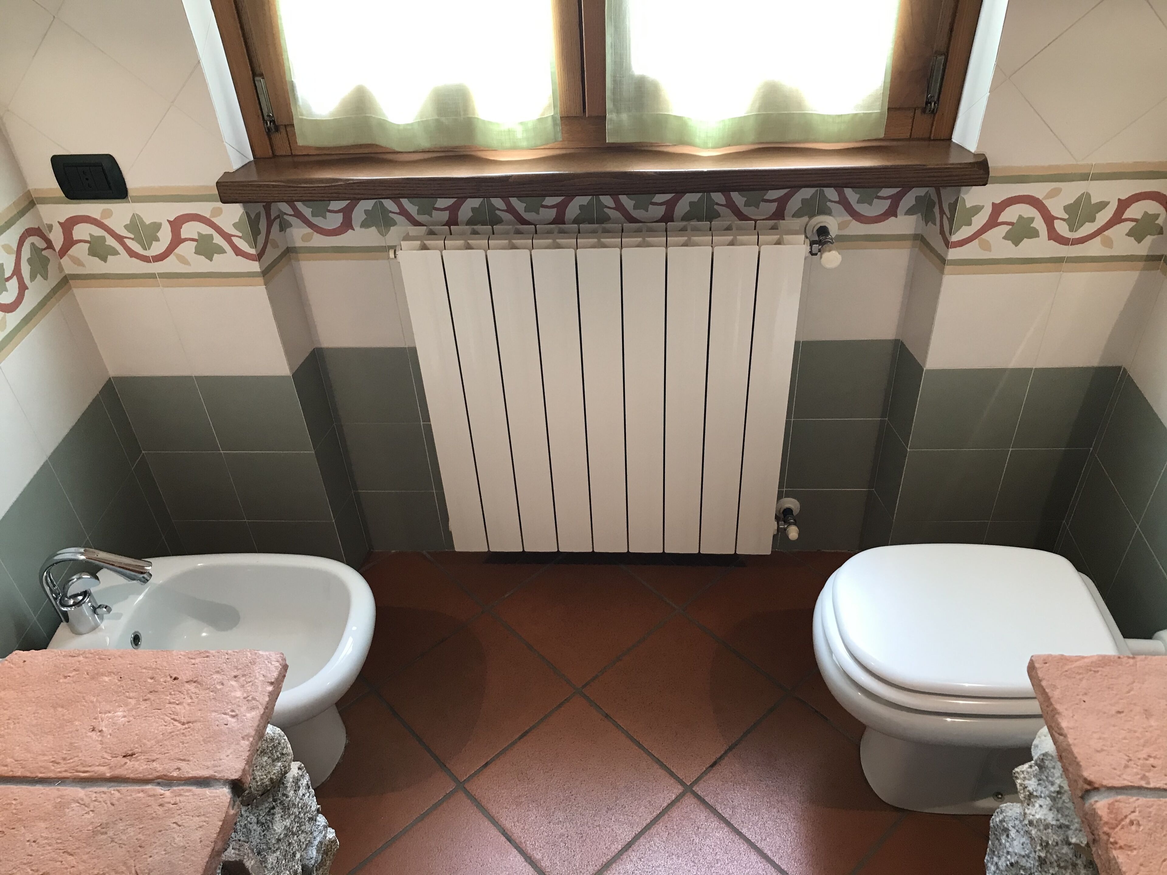Une salle de bain équipée d’un bidet, de toilettes et d’une fenêtre avec un rideau.
