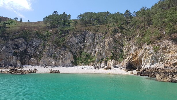 A coastal landscape with clear turquoise waters, rocky cliffs, and a sandy beach.