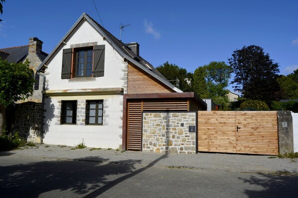 Una casa de dos pisos con fachada de piedra, tejado inclinado de madera y entrada con portón.