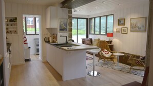 A modern kitchen with a central island, a dining area with wicker furniture, and large windows offering views of the outdoors.