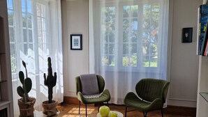 A living room with wooden flooring, two green armchairs, a small table with a yellow vase, and two potted cacti. - Entre Terre et Mer (Plougoulm)