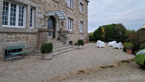 A stone building with a gravel courtyard, a bench, potted plants, and white outdoor furniture. - Entre Terre et Mer (Plougoulm)