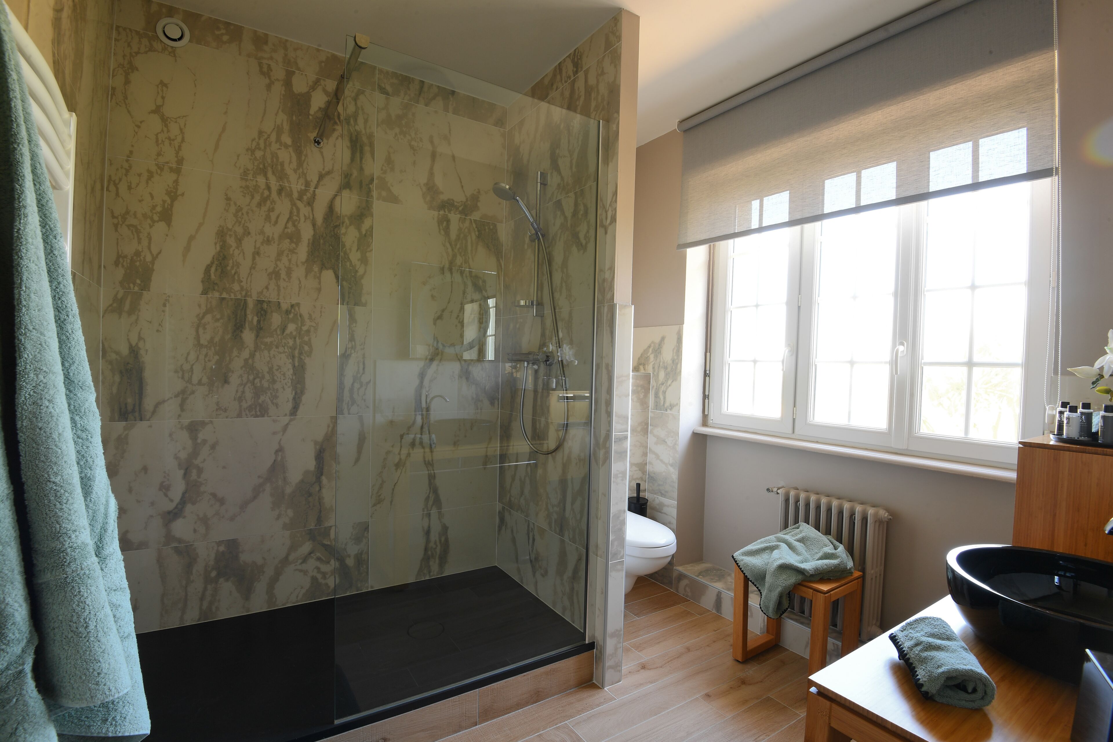 A modern bathroom with a glass-enclosed shower, a toilet, a sink, and a window providing natural light.