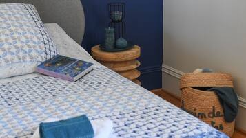 Een keurig opgemaakt bed met een bedsprei met dessin, een boek en een klein houten nachtkastje met kandelaar.