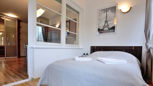 A neatly made bed with a grey bedspread and white towels, a large window with multiple panes, and a framed picture of the Eiffel Tower on the wall. - Victus Apartamenty - Petit (Sopot)