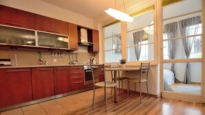 A modern kitchen with wooden cabinets, a dining area with a table and chairs, and a large window with curtains. - Victus Apartamenty - Petit (Sopot)