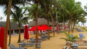 Un resort frente a la playa con cabañas de techo de paja, palmeras y tumbonas.