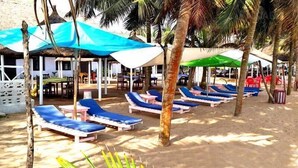 Un resort frente a la playa con tumbonas bajo sombrillas, palmeras y una zona de piscina.