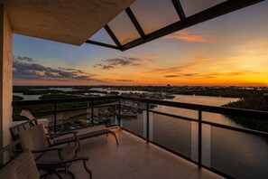 A balcony with chairs and a view of a river at sunset.