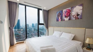 Een hotelkamer met een groot bed, een nachtkastje en een stadszicht door grote ramen.