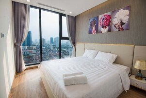 Habitación de hotel con una cama grande, una mesita de noche y vistas a la ciudad a través de amplios ventanales.