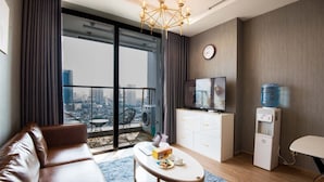 Een moderne woonkamer met een leren bank, een salontafel, een televisie, een waterdispenser en uitzicht op de stad door grote ramen.