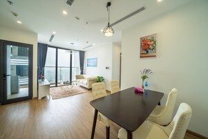 Una sala de estar moderna con una mesa de madera oscura, sillas color crema, un ventanal con vistas y un cuadro en la pared.