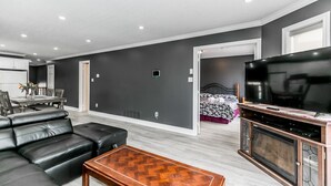 A modern living room with a black leather sofa, a wooden coffee table, a flat-screen TV, and a dining area with a table and chairs. - Beach1 Riverfront Resort - #32 - Wasaga Beach (Wasaga Beach)