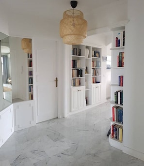 A hallway with white walls, a marble floor, and bookshelves filled with books.