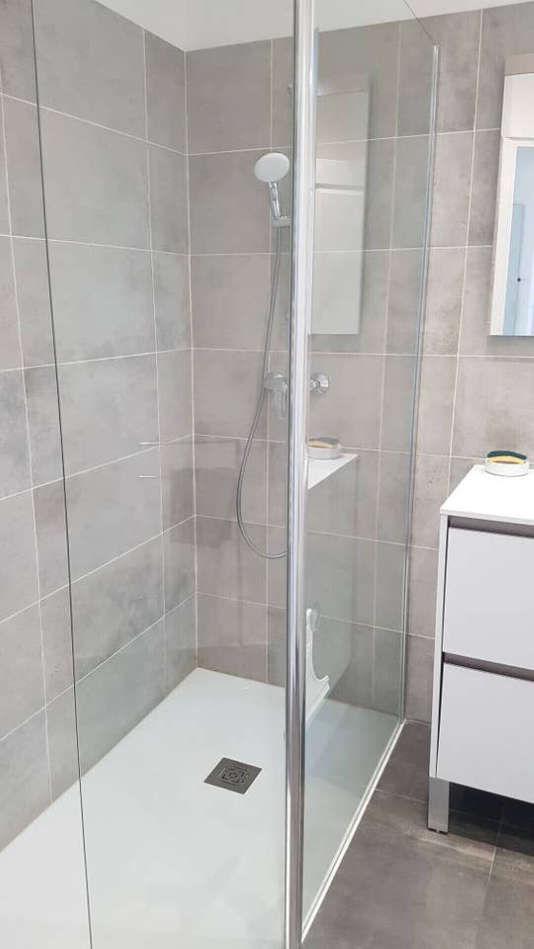 A modern bathroom with a glass-enclosed shower, a white sink, and a mirror above it.