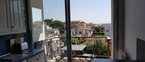 A balcony with a view of a residential area, a table, chairs, and a kitchen area with cabinets and a toaster.