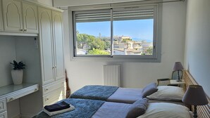 Ein Schlafzimmer mit zwei Betten, einem Schreibtisch und einem Fenster mit Blick auf Gebäude und Bäume.