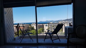 Ein Balkon mit zwei Stühlen und einem Tisch, mit Blick auf eine Stadtlandschaft und das Meer.