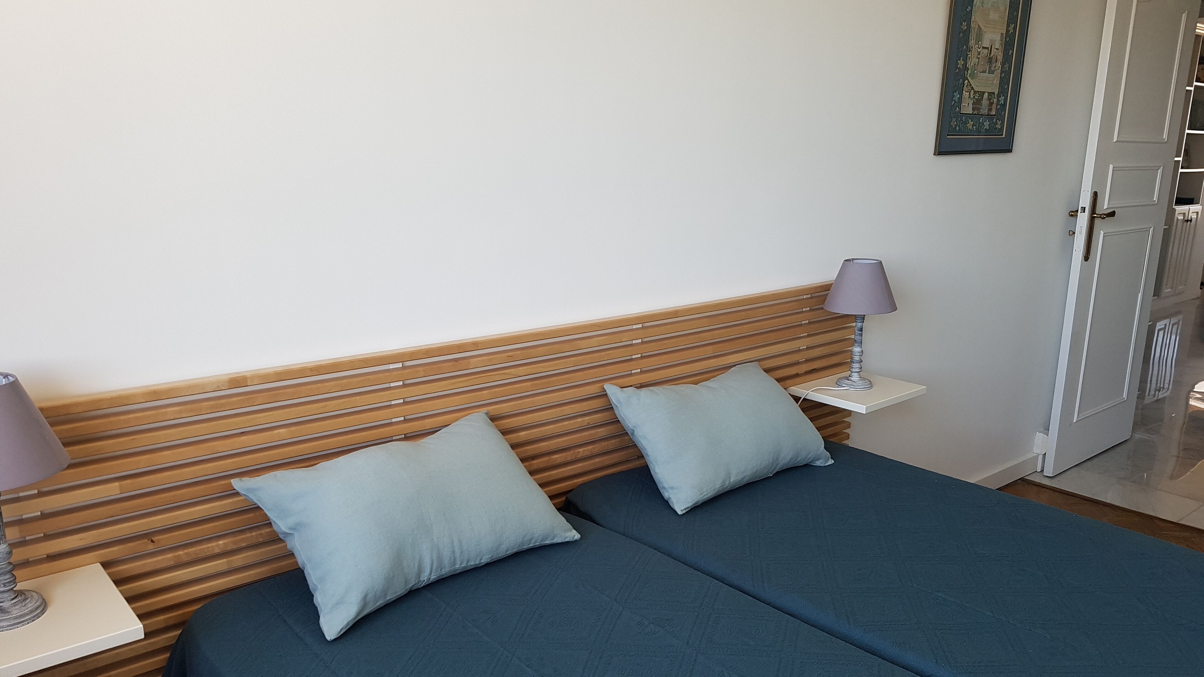 A room with a bed, two pillows, a nightstand with a lamp, and a door.