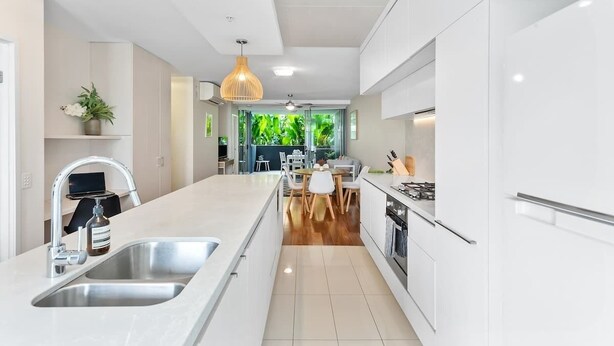 A modern kitchen with white cabinetry, a central island with a sink, and a dining area with a table and chairs.