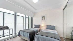 A hotel room with two beds, a desk, a lamp, and a large window.