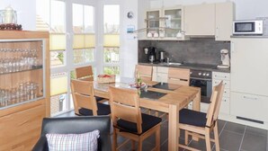 A modern kitchen with a dining area, featuring a wooden table, chairs, and a glass cabinet with glasses. - Seetiger (Krummhoern)