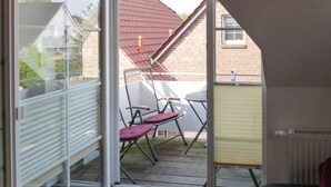 A balcony with a glass door, a red roof visible through the door, and a small table with chairs. - Seetiger (Krummhoern)