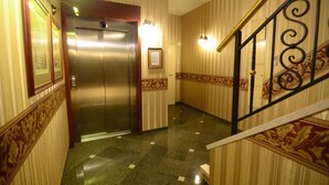 Un pasillo de hotel con un ascensor metálico, una escalera con barandilla decorativa y diseños de pared estampados.