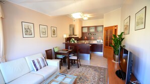Una sala moderna con un sofá, una mesa de centro y una zona de comedor con sillas y una mesa. Se ve una cocina al fondo, con armarios y un microondas.