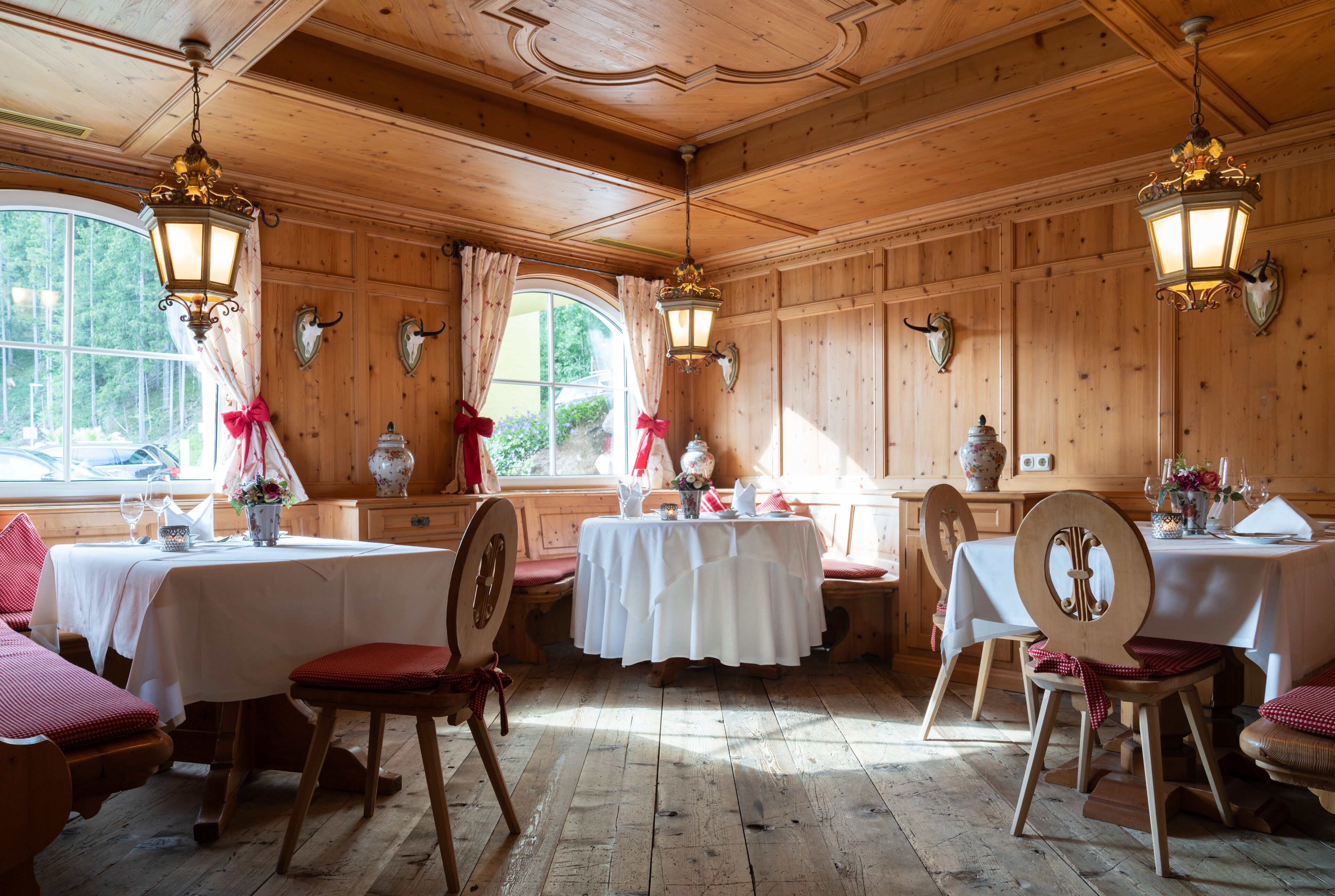 Una habitación con paneles de madera, con mesas dispuestas para comer, manteles blancos y cojines rojos.