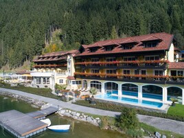 Un hotel con piscina, un muelle y un barco, con un paisaje boscoso al fondo.