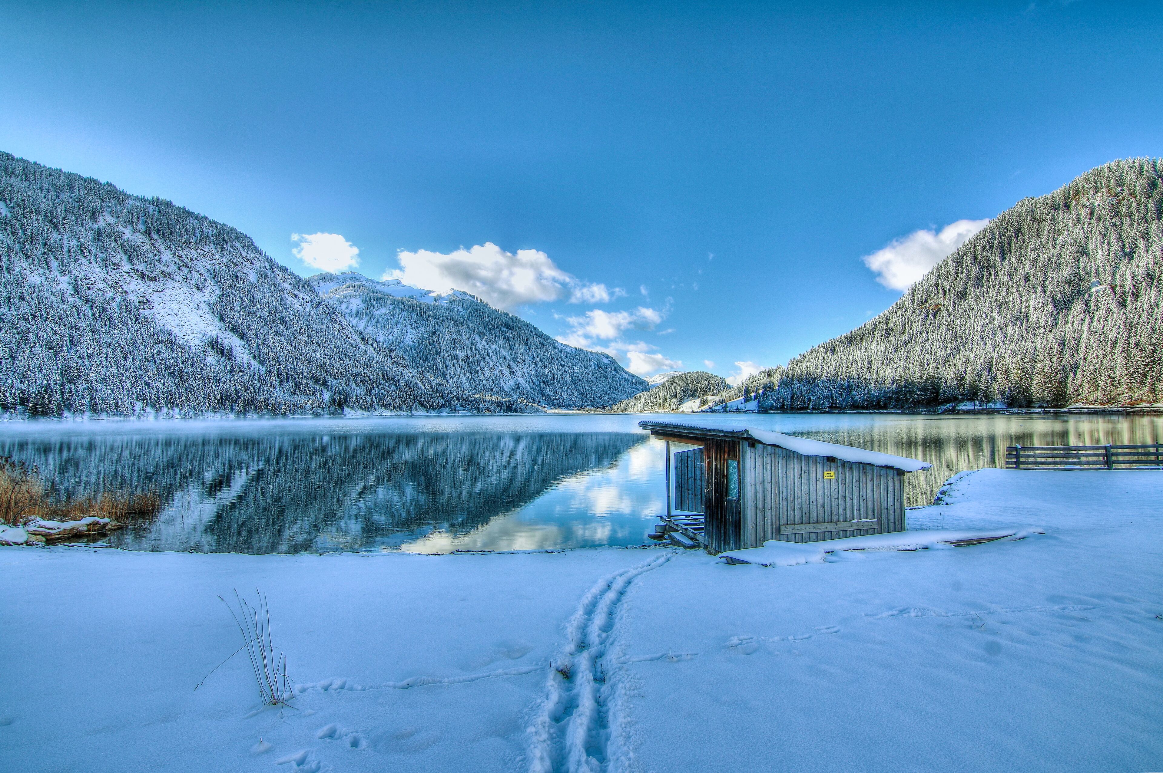 Una cabaña junto a un lago tranquilo con montañas nevadas al fondo.