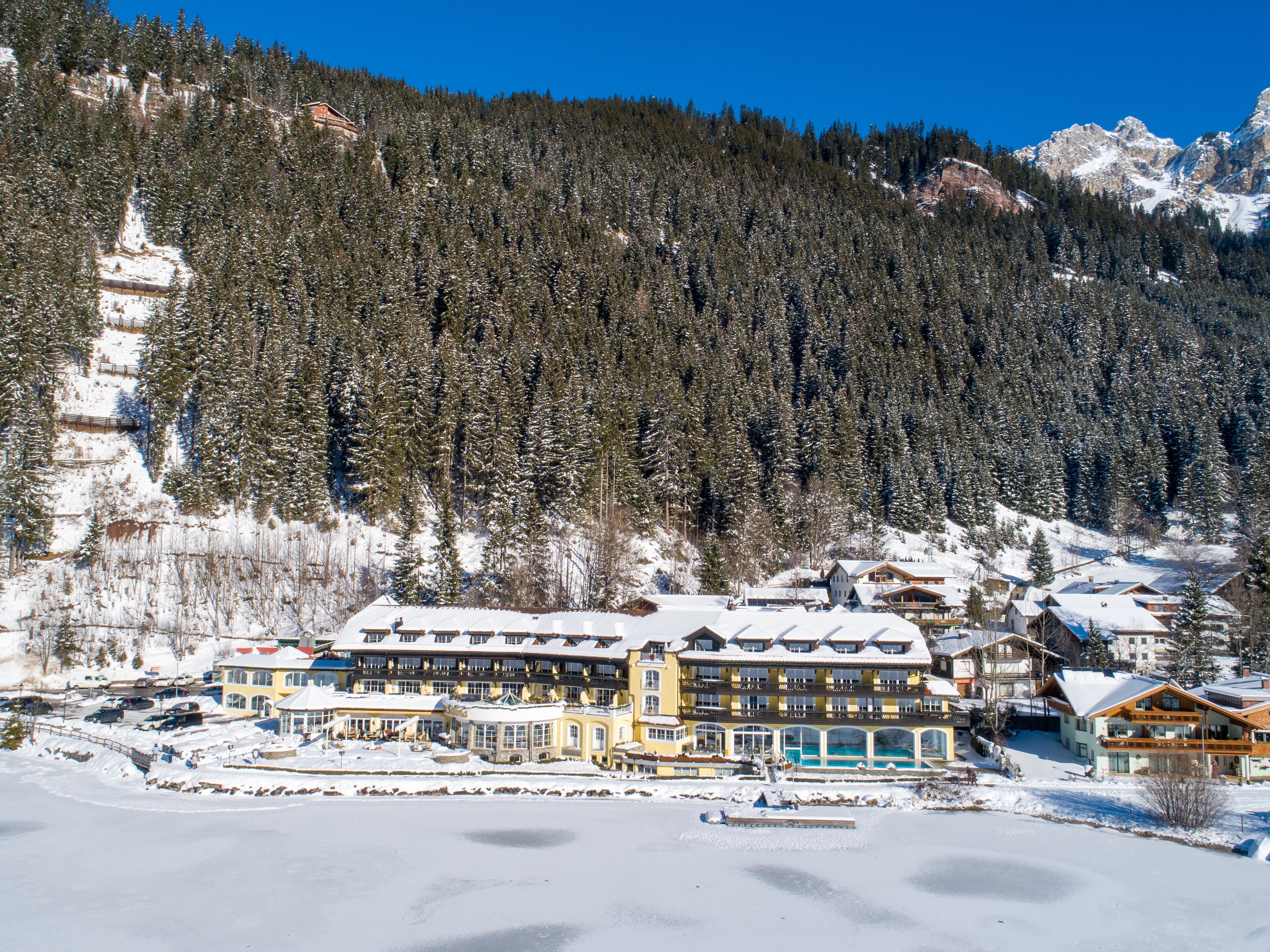 Ein großes, mehrstöckiges Hotel mit schneebedecktem Dach, eingebettet in eine bewaldete Berglandschaft.