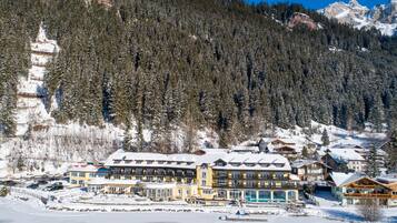 Ein großes, mehrstöckiges Hotel mit schneebedecktem Dach, eingebettet in eine bewaldete Berglandschaft.