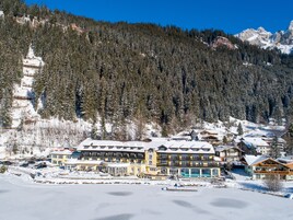 Un hotel grande de varios pisos con techo nevado, rodeado por un paisaje montañoso cubierto de bosque.