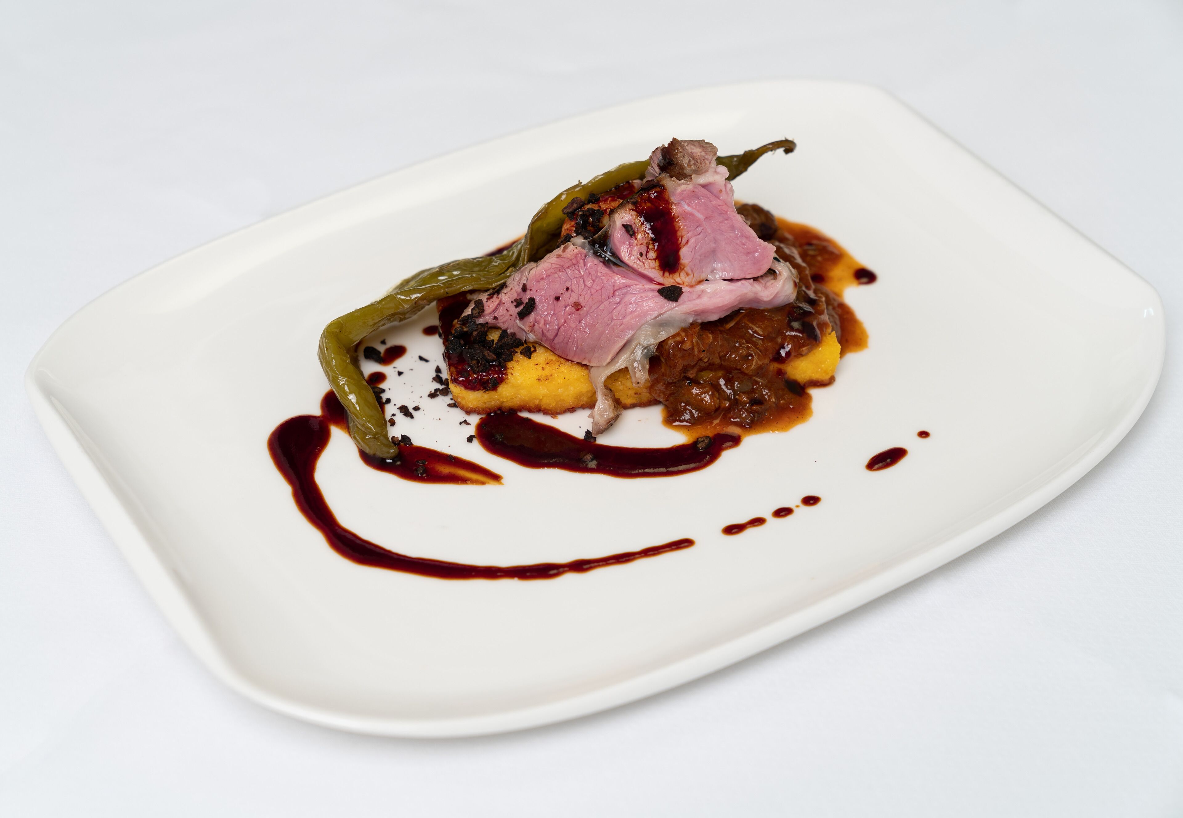 A white plate with a dish consisting of meat, vegetables, and sauce.