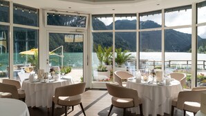 Un espace repas avec des tables préparées pour deux personnes, de grandes fenêtres offrant une vue sur les montagnes et un balcon donnant sur le lac.